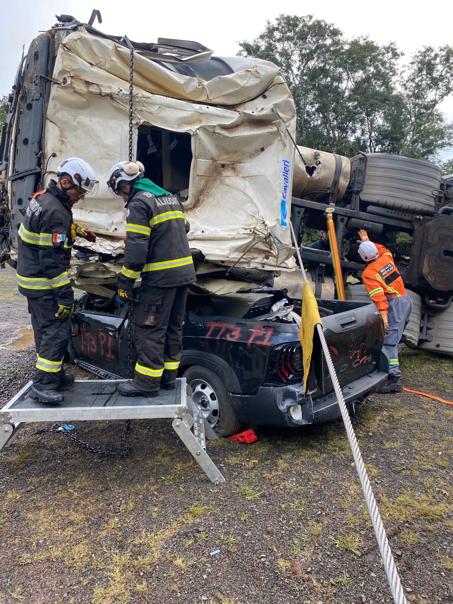 Rescatistas acondicionan el izaje con cadenas junto a la cabina volcada de un camión sobre un vehículo liviano, durante un entrenamiento de rescate vehicular pesado